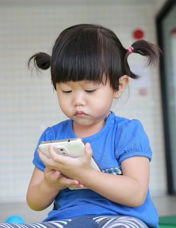Cute asian baby girl age about one year old and nine month playing a smartphone at the Kid roomの写真素材