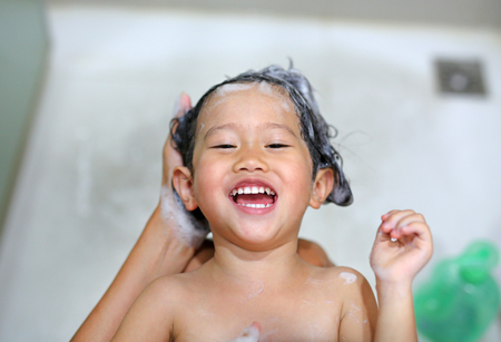 Cute little girl is being bathed and shampooed by her mother.の写真素材