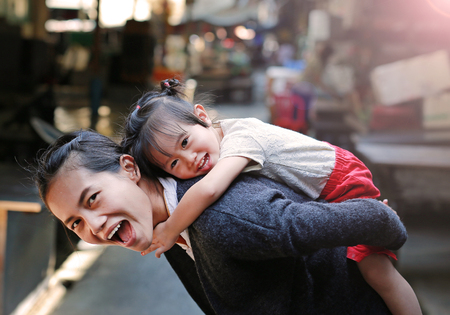 Happy family, Portrait of cute little girl riding on mother back in Bangkok Thailand.の写真素材