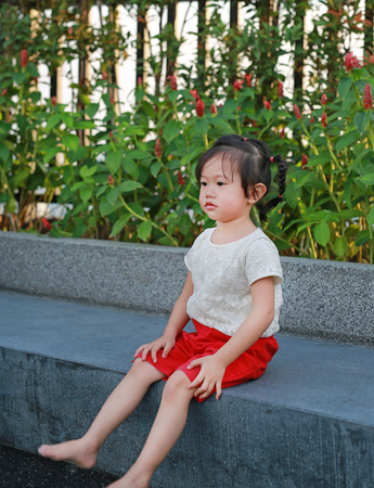 Cute little asian girl sitting on stone bench in the garden.の写真素材