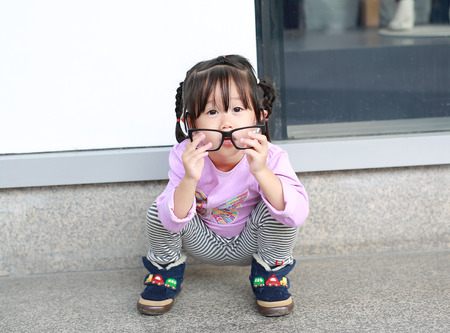 Portrait of cute little girl trying to wear glassesの写真素材