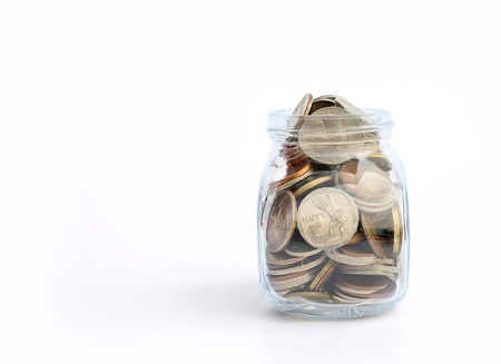 International coins in a glass jar on white background with copy space.