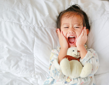Asian little girl with teddy bear lying on bedの写真素材