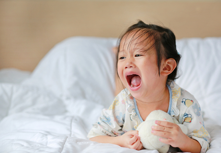 Asian little girl with teddy bear lying on bedの写真素材