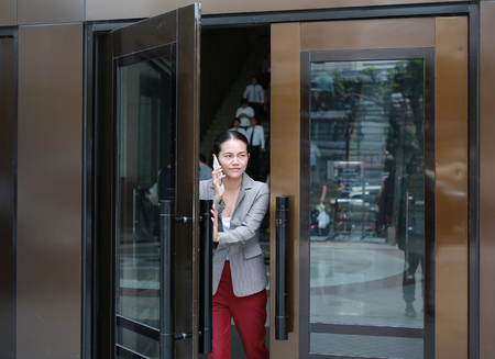 Beautiful young business woman using telephone with open door and walking outside.の写真素材