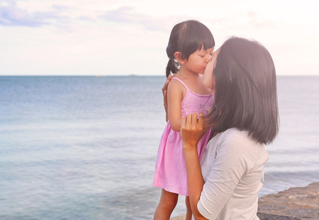 mother and kid girl kissing with natural emotion smiling on sea background in the eveningの写真素材