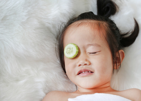 Cute little Child girl with a slice of cucumber in her eye, concept for skin care.の写真素材