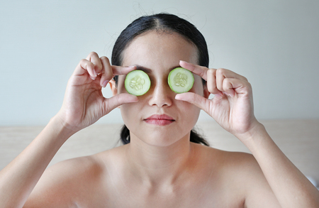 Portrait of a young beautiful woman holding cucumber slices on her eyes.の写真素材