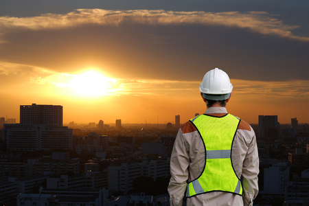 Back view of Male construction worker against building at sunset in bangkok city backgroundの写真素材