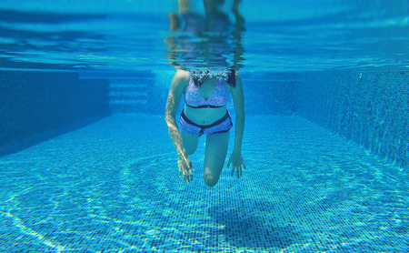 Underwater shot of young woman diving into the swimming pool.の写真素材