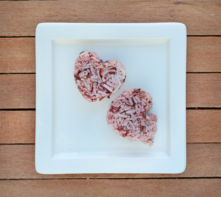 Brown rice in heart shape on square ceramic plate against plank wood backgroundの写真素材