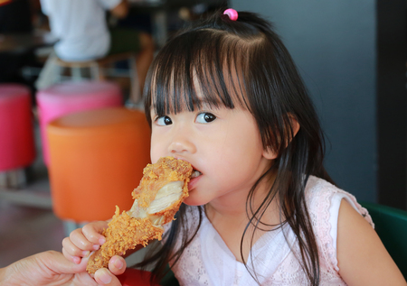 Close up of little asian girl eating fried chicken in cafe.の写真素材