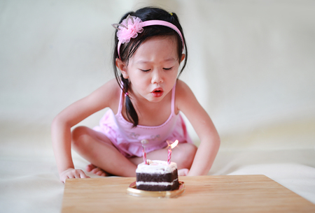 Cute little girl blowing small birthday candles on cake, 2 years old kid celebratingの写真素材
