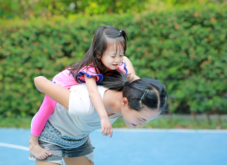 Happy family, Portrait of cute little girl riding on mother back in the parkの写真素材
