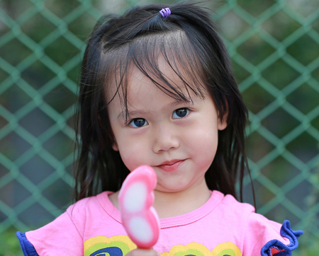 Happy little child girl eating ice-cream in the park against iron mesh background