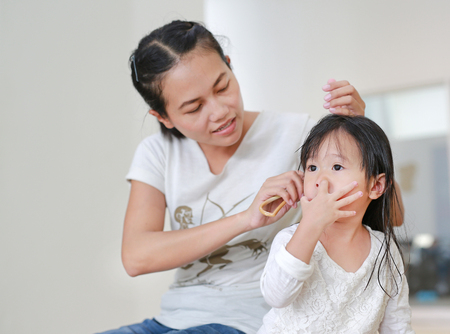 Baby care after bathing, mother is combing daughter's hair with funny face of her daughterの写真素材