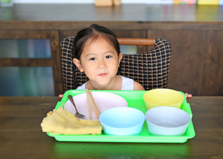 Little Asian girl waiting food at the table with many empty bowlの写真素材