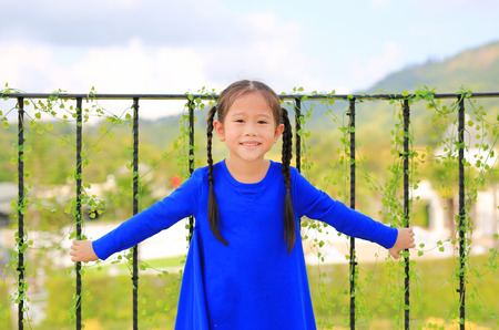 Smiling little girl standing at balcony bars and looking camera at the morning.の写真素材