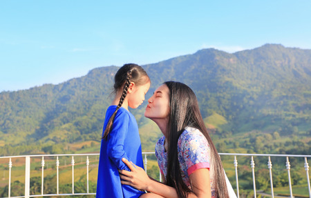 Asian mother and daughter kissing on balcony at hillside.の写真素材