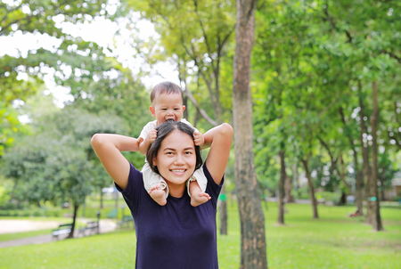 Beautiful young Asian mother with happy baby boy riding on mom's shoulder in the nature park.の写真素材