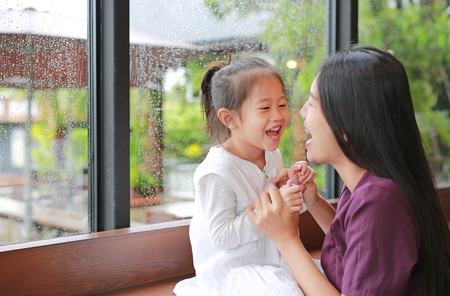 Asian mother and her daughter playing with love near a window while raining day.