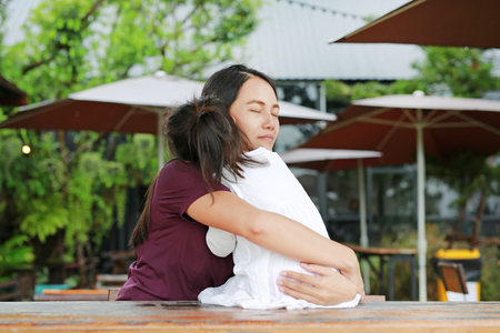 Asian mother embracing her daughter with love on the wood table at outdoor restaurant.の写真素材