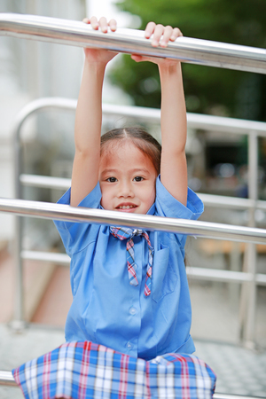 Smiling little Asian girl in school uniform playful hanging at metal stair.の写真素材