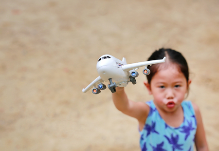 Adorable little Asian child girl playing with a toy airplane in the garden.