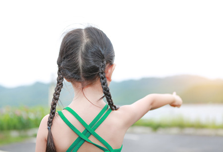 Little Asian child girl pointing up in summer field outdoor. Freedom style outdoor.の写真素材