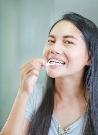 Smiling Asian women using dental floss for healthy teeth.