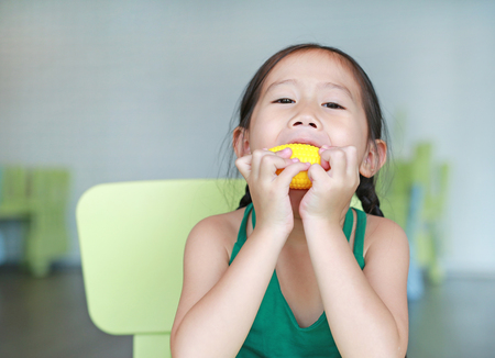 Adorable little Asian child girl playing to eating plastic corn in kid room.の写真素材