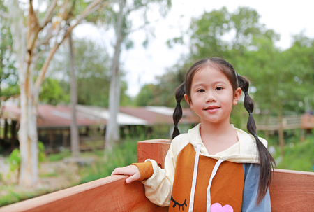 Adorable little Asian child girl in warm clothes standing on balcony in the garden.の写真素材