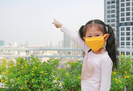 Asian child girl wearing a protection mask against PM 2.5 air pollution with pointing up in Bangkok city. Thailand.の写真素材