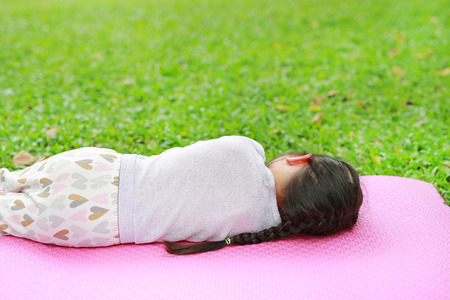 Rear view little Asian child girl sleeping on pink mattress in green grass lawn at summer park garden.の写真素材