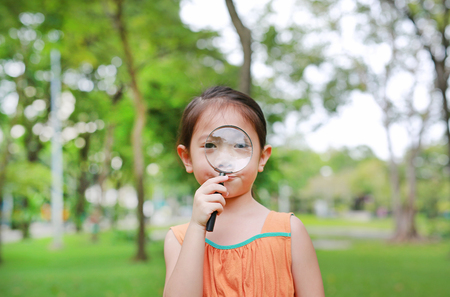 Portrait little Asian child girl looking through magnifying glass on park garden.の写真素材