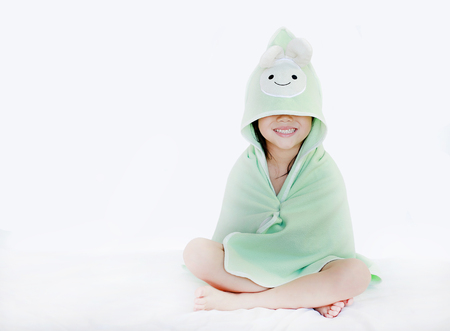 Portrait of smiling Asian child girl after bath covered head and eyes with towel. Funny kid in towel sitting on white background.の写真素材