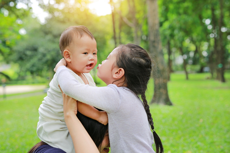 Close up baby boy riding on mom's shoulder with sister kissing in the nature park.の写真素材