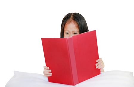 Beautiful little Asian child girl reading hardcover book lying with pillow on white background.の写真素材