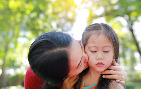Close up asian mother kissing her daughters lying in the summer garden.の写真素材