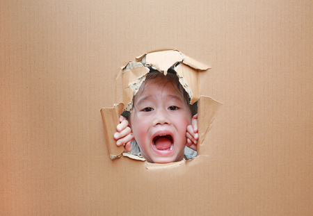 Happy Asian kid girl looking through hole on cardboard with copy space.の写真素材