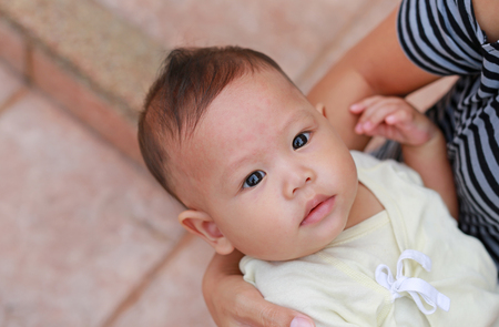 Close-up Asian baby boy lying in hug of mother with looking camera.の写真素材