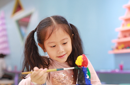 Happy little child girl having fun to paint on stucco doll indoor.の写真素材