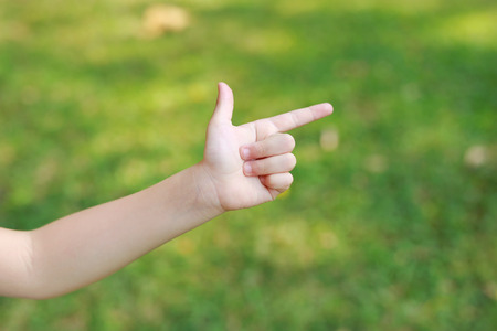 Children hand pointing with index finger or making gun gesture on blur green garden background. Kid hand show up forefinger correct or point.の写真素材
