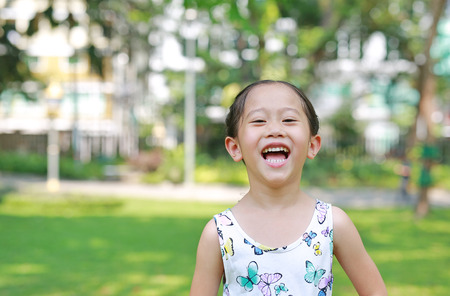 Portrait of happy little Asian child girl in sunny green park.
