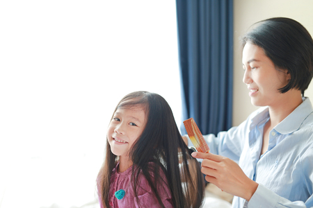 Beautiful little Asian child girl with long hair and mom dressed up for Smooth hair at morning in the room.の写真素材