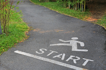 Sign running and word start at point on the asphalt street in park.