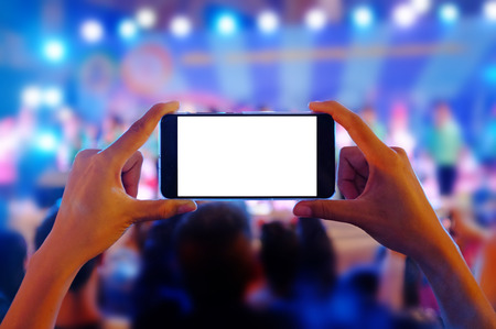 Hands holding a mobile smartphone records colorful live concert with blank white screen.
