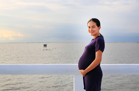 Beautiful pregnant woman standing on seashore with looking at camera.の写真素材