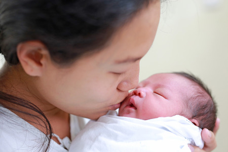 Closeup mother kissing infant baby in her arms in hospital after delivery room.