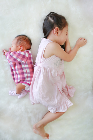 Asian older sister and newborn baby boy sleeping together on white fur background.の写真素材